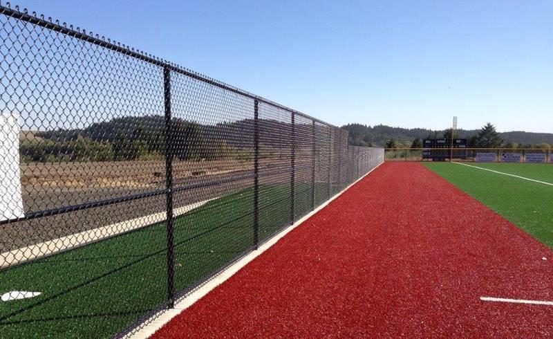 Black chain link fence running alongside the track at a sports field